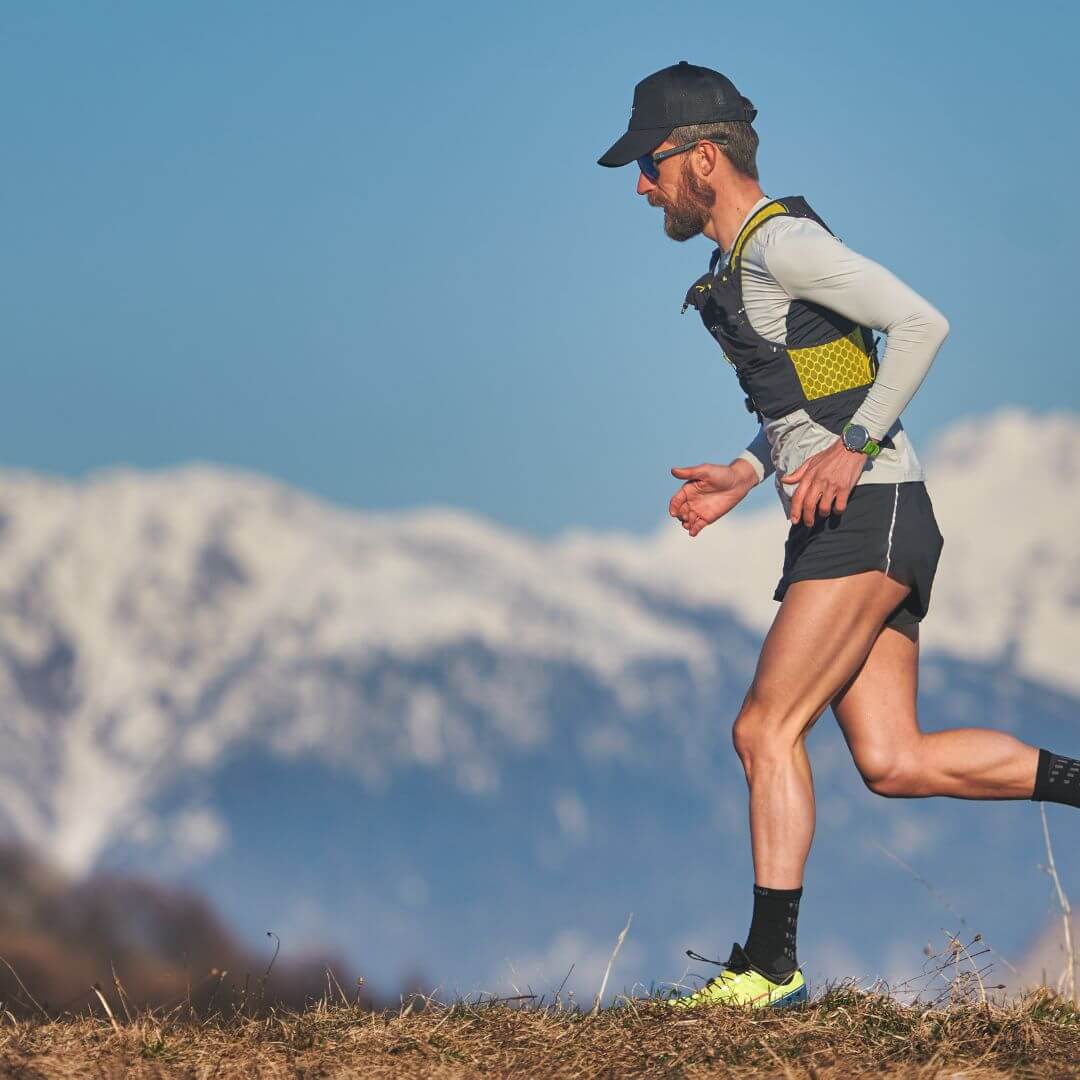 Man running on a trail with snow capped mountains in the background