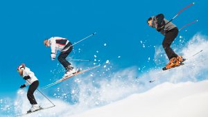 three downhill skiers with powder and blue sky